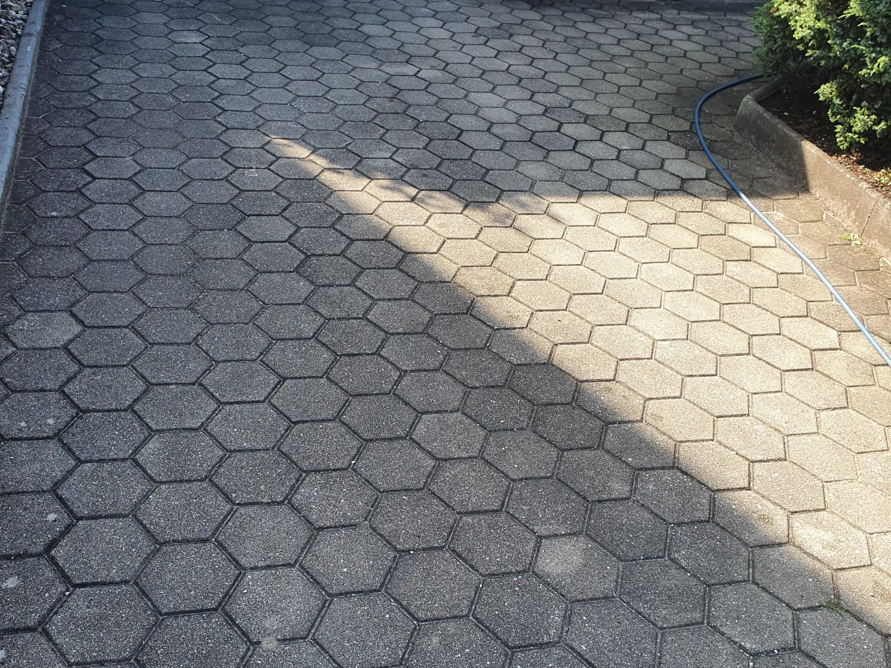 Sechseckiges Betonpflaster einer Hauszufahrt, zur Hälfte gereinigt, mit klarer Kante zum verschmutzten Bereich.