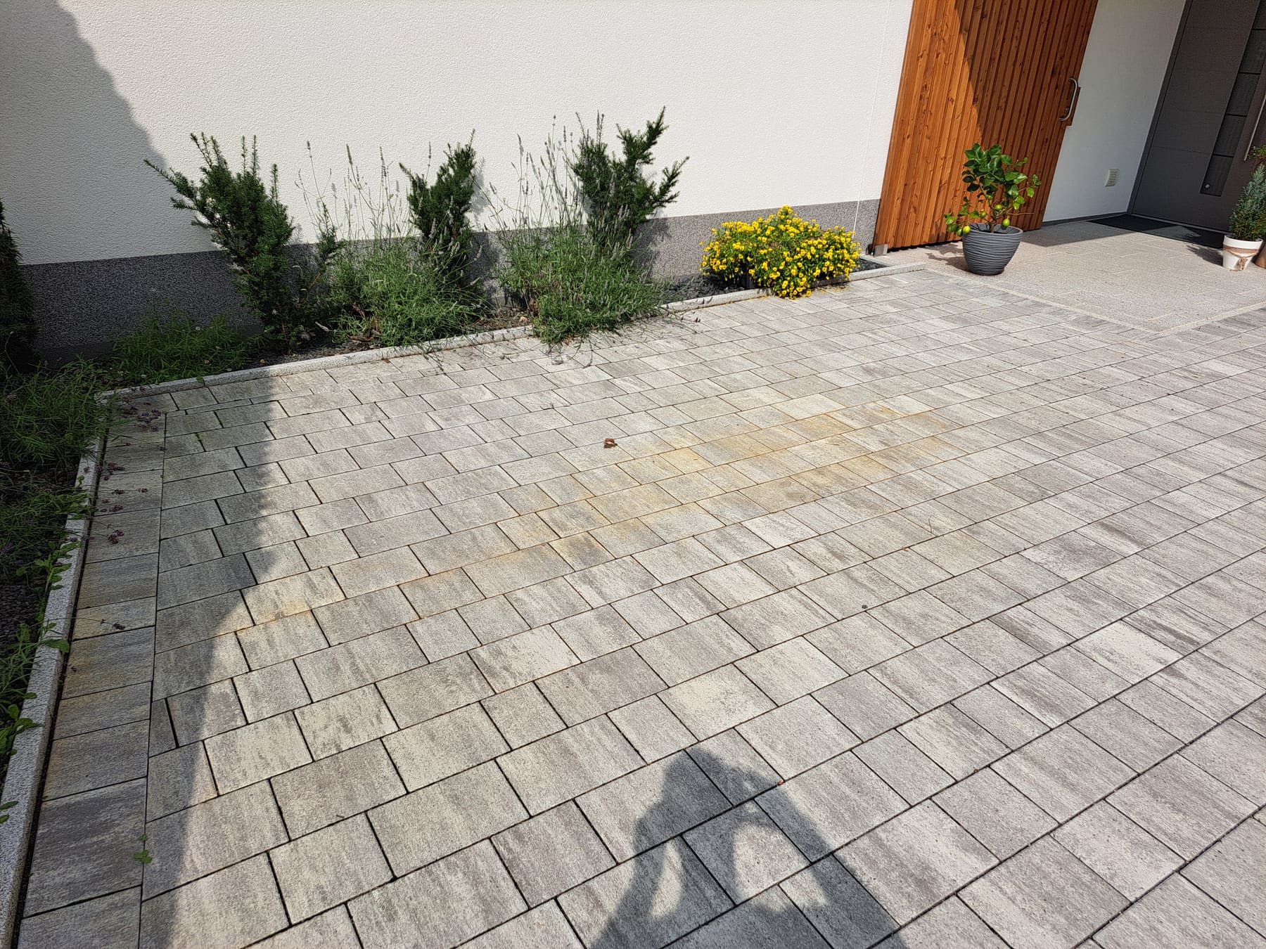 Betonsteinfläche vor einem Hauseingang mit orangebraunen Rostverfärbungen im mittleren Bereich.