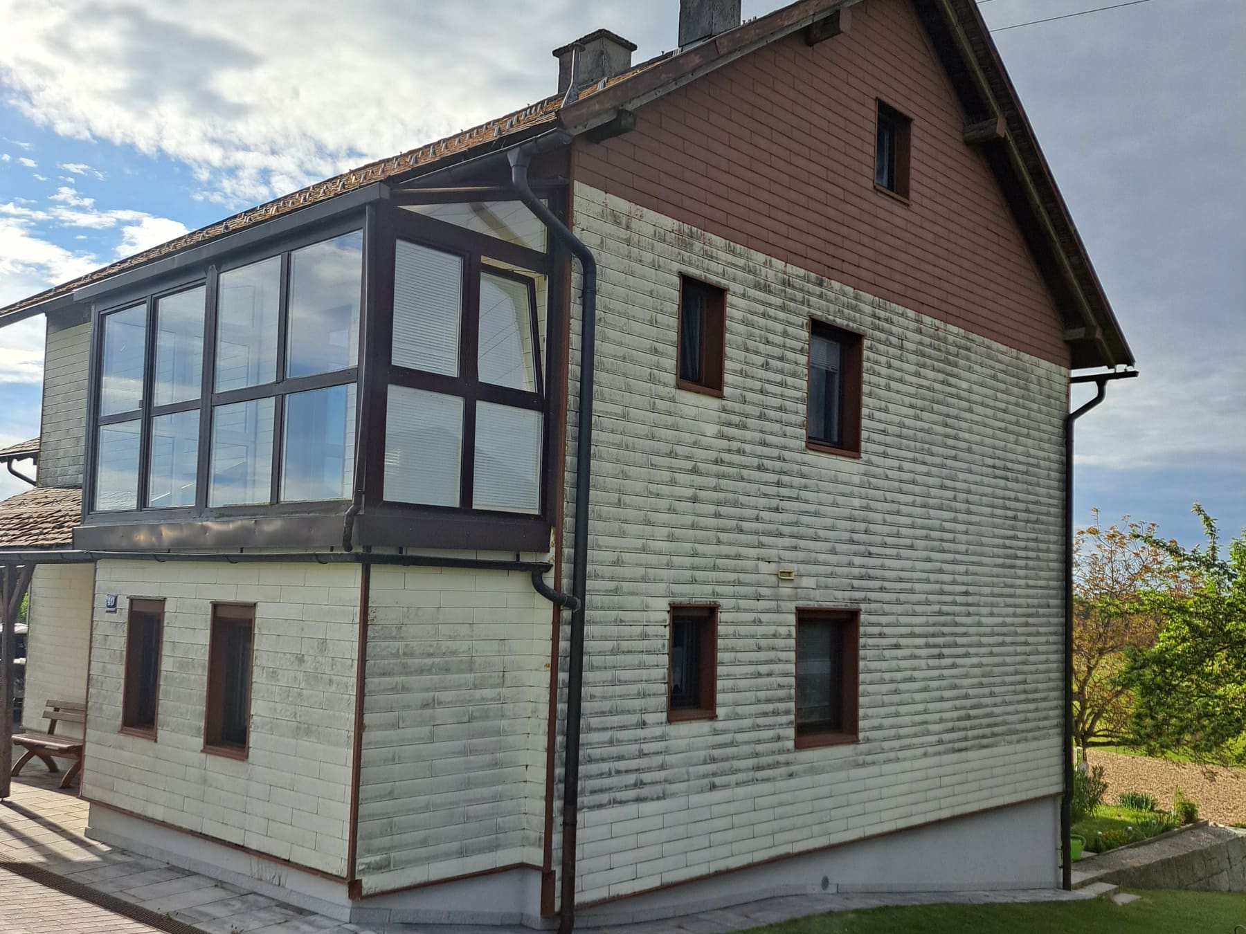 Faserzementfassade eines Wohnhauses vor der Reinigung, mit streifigen Verschmutzungen zwischen den Platten.