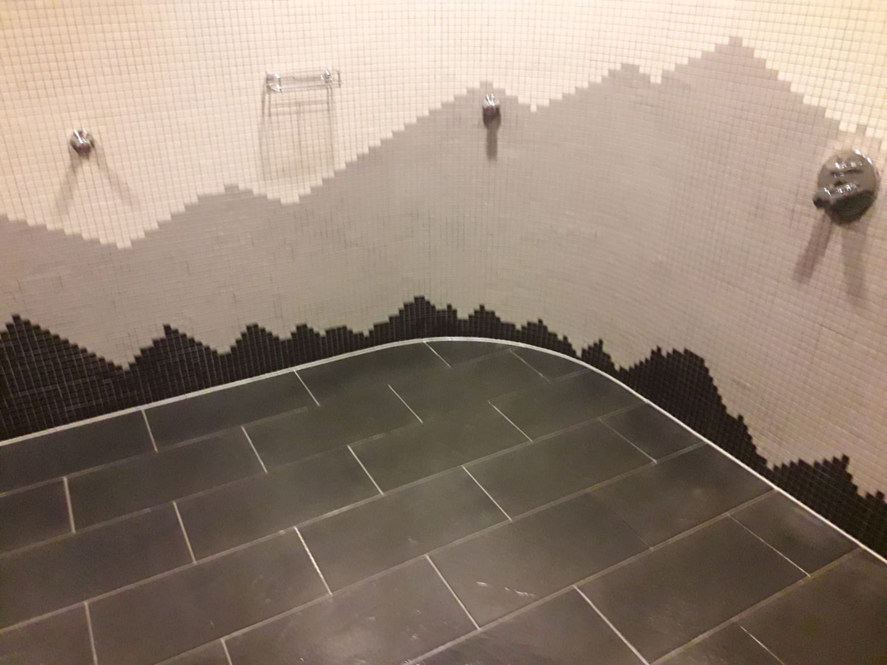 Mosaikfliesen in einem Nassbereich, zur Hälfte gereinigt – die Reinigungsgrenze ist deutlich sichtbar.