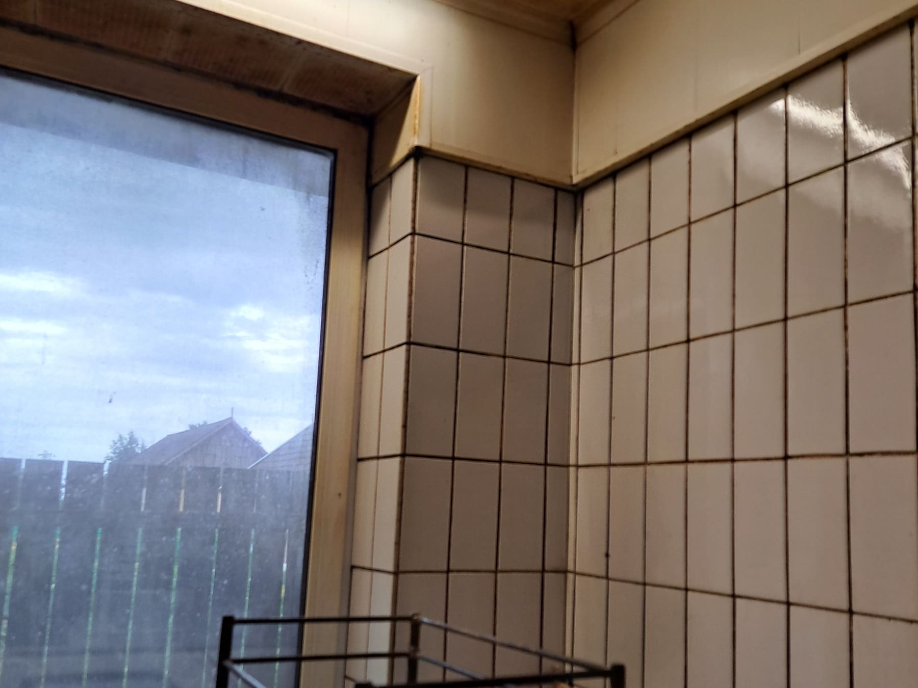 Ecke einer gewerblichen Küche vor der Reinigung, mit vergilbter Decke und fettbelegten Wandfliesen.