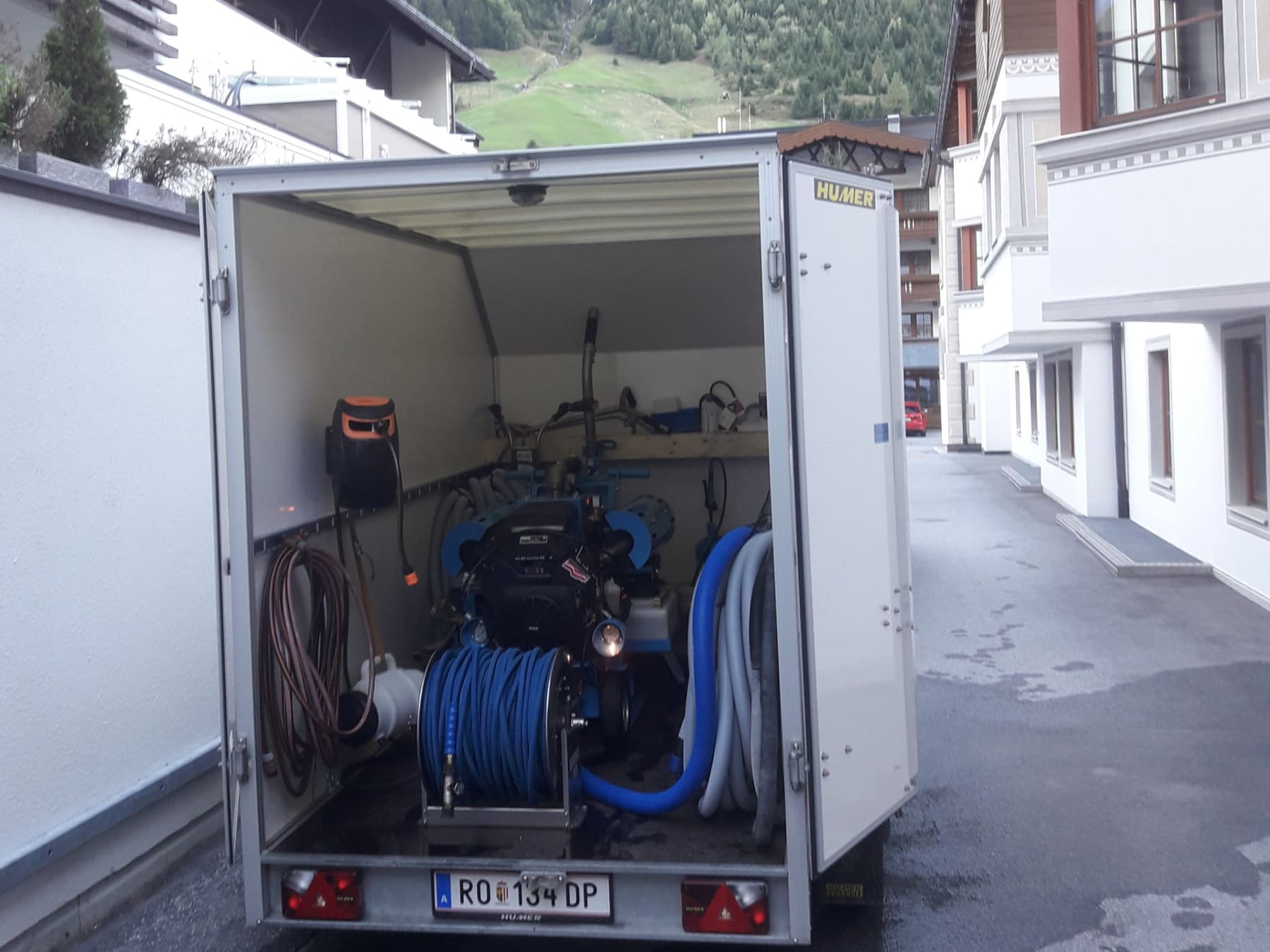 Geöffneter Geräteanhänger mit Warmwasser-Saugmaschine, Schlauchtrommeln und Zubehör.
