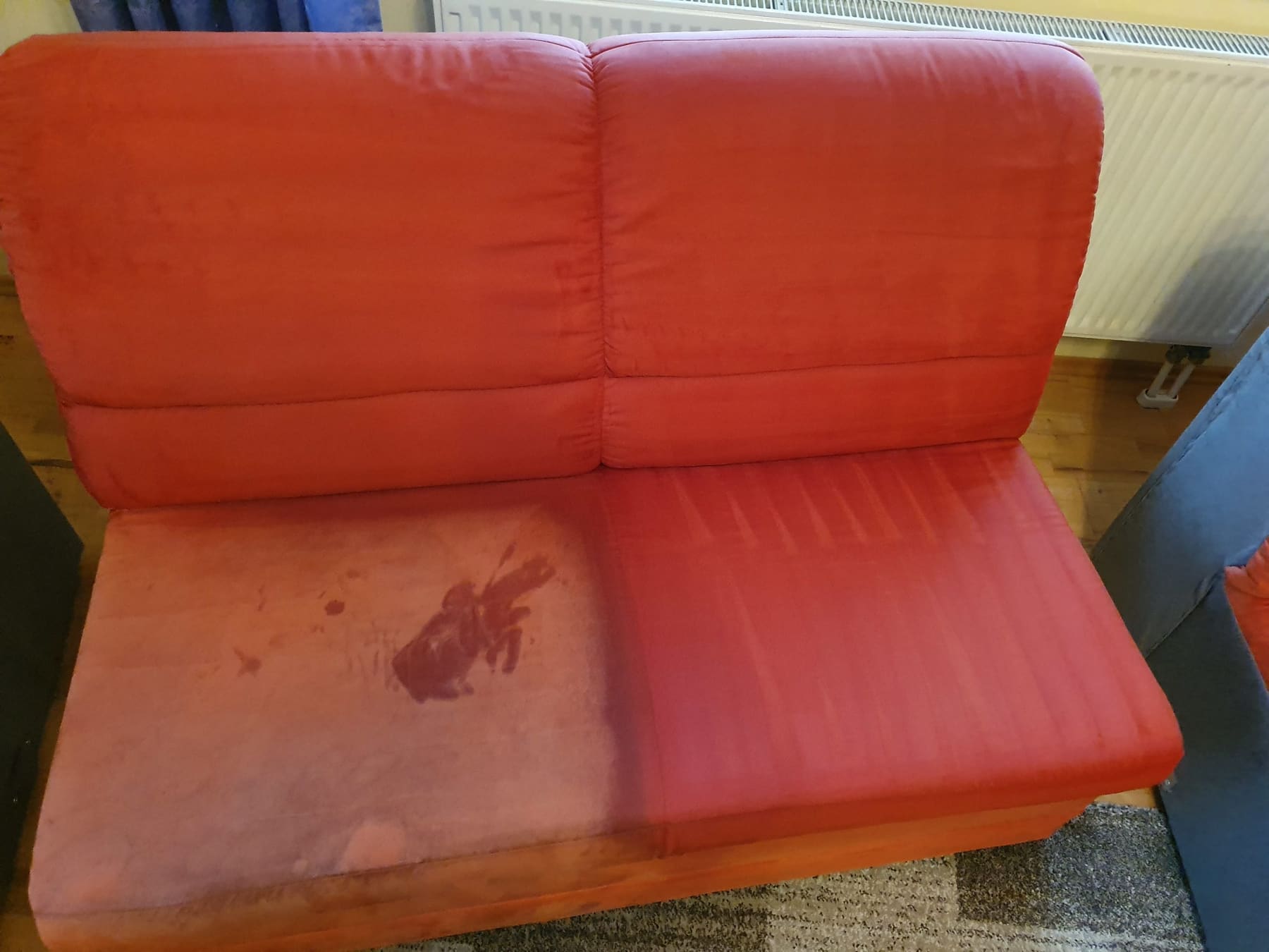 Rotes Polstersofa, zur Hälfte gereinigt – der behandelte Bereich ist deutlich heller.