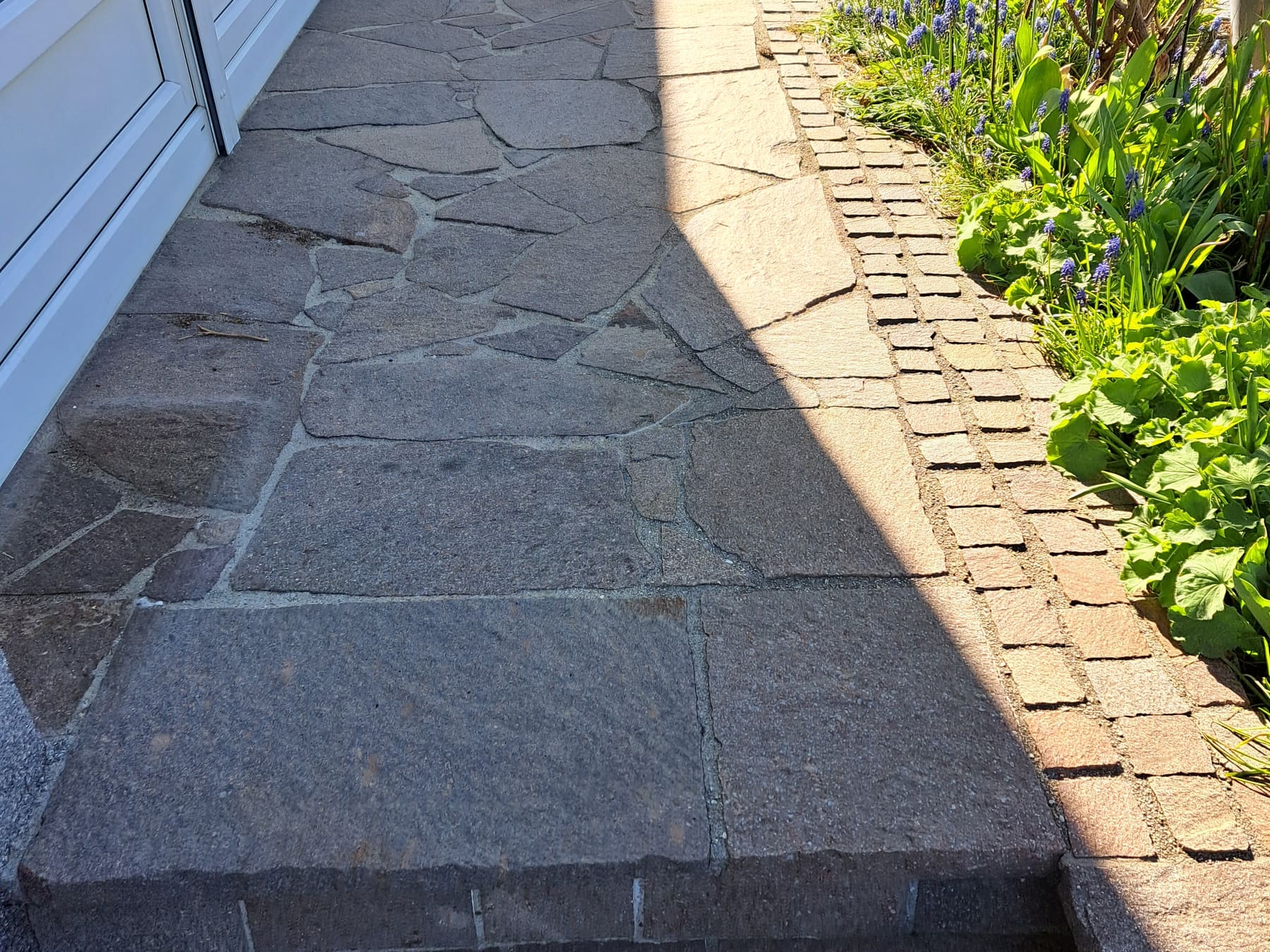 Porphyr-Plattenweg entlang einer Hausfront vor der Behandlung, mit stumpfer, grau wirkender Oberfläche.