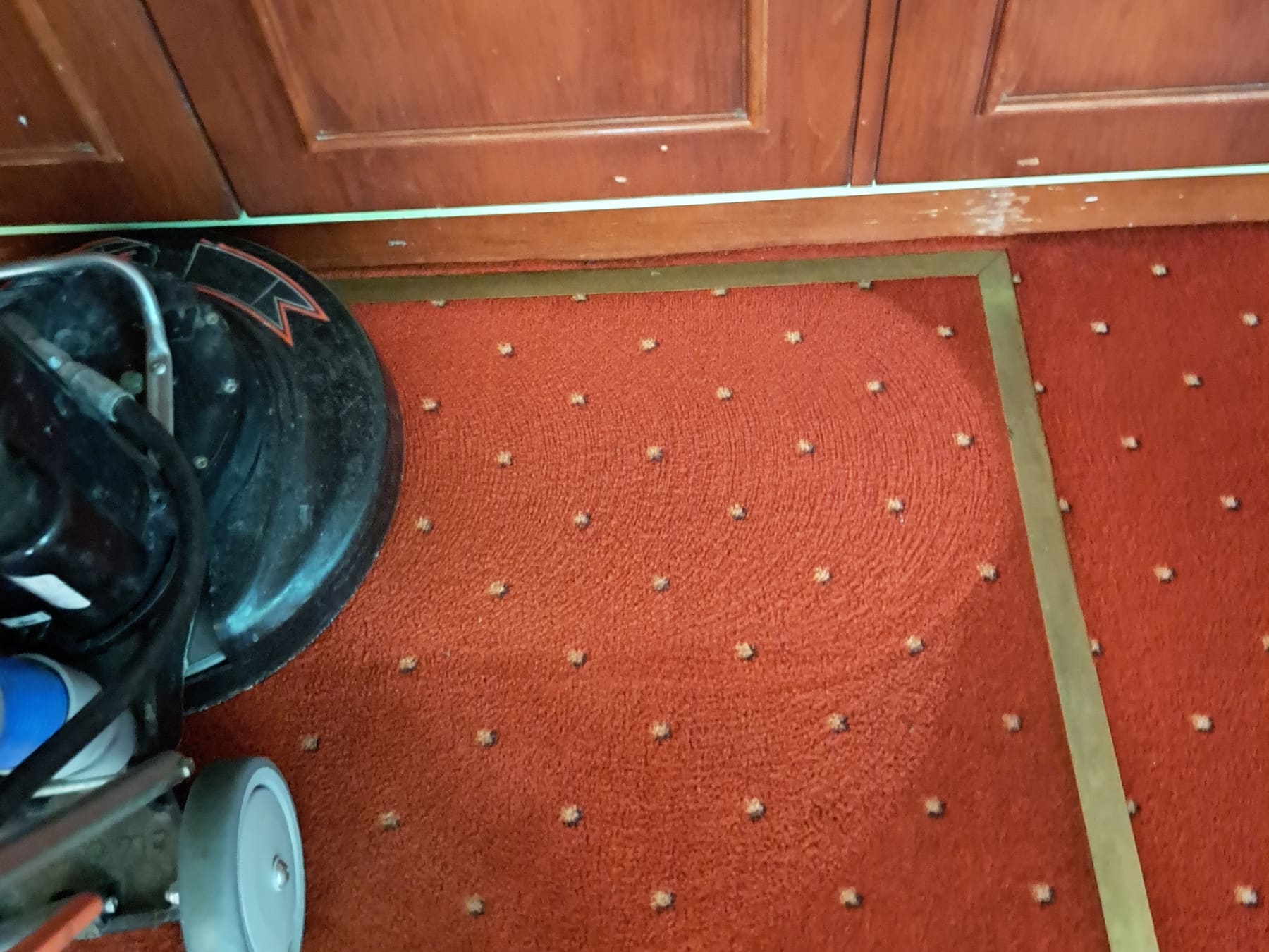 Roter Objektteppich mit abgeklebter, bereits gereinigter Probefläche und der eingesetzten Reinigungsmaschine.